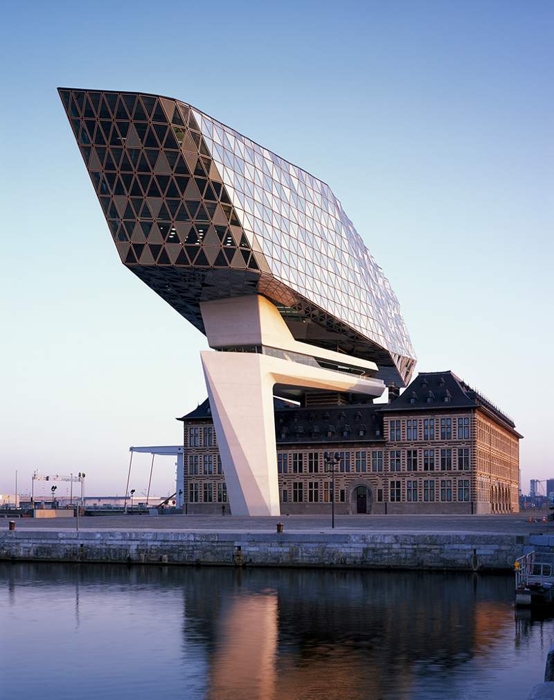 O escritório de arquitetura de Zaha Hadid acabou de inaugurar o novo Port House de Antuérpia, na Bélgica. Essa nova construção usa da estrutura base de uma antiga sede dos bombeiros na zona portuária da cidade e acabou transformando o edifício no centro para os mais de 500 funcionários que trabalhavam em prédios separados pela cidade. A construção foi feita em forma de uma extensão elevada que parece flutuar sobre o edifício original. Sua fachada é feita de vidro com a intenção de refletir as cores do céu e seu formato é inspirado nos navios que cruzam essa cidade belga todos os dias. 