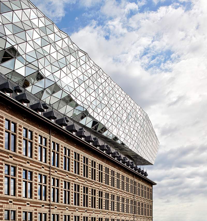 O escritório de arquitetura de Zaha Hadid acabou de inaugurar o novo Port House de Antuérpia, na Bélgica. Essa nova construção usa da estrutura base de uma antiga sede dos bombeiros na zona portuária da cidade e acabou transformando o edifício no centro para os mais de 500 funcionários que trabalhavam em prédios separados pela cidade. A construção foi feita em forma de uma extensão elevada que parece flutuar sobre o edifício original. Sua fachada é feita de vidro com a intenção de refletir as cores do céu e seu formato é inspirado nos navios que cruzam essa cidade belga todos os dias. 