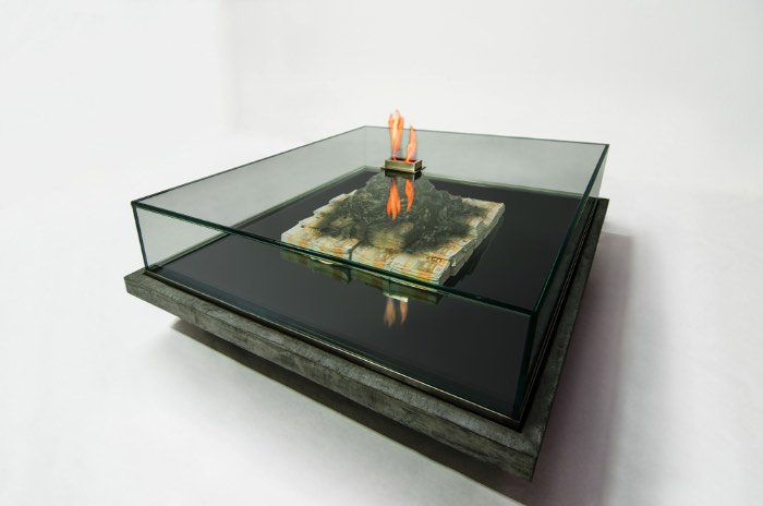 As imagens que você pode ver nesse artigo é uma colaboração artística entre Alejandro Monge e Amarist Studio para a série chamada de Too Much. O objetivo dessa estranha escultura em forma de mesa de café é questionar o real valor do dinheiro e a volatilidade de toda a riqueza financeira. O resultado desse questionamento é um objeto de arte refinado que é feito de notas de 50 euros que queimam embaixo de uma superfície de vidro.