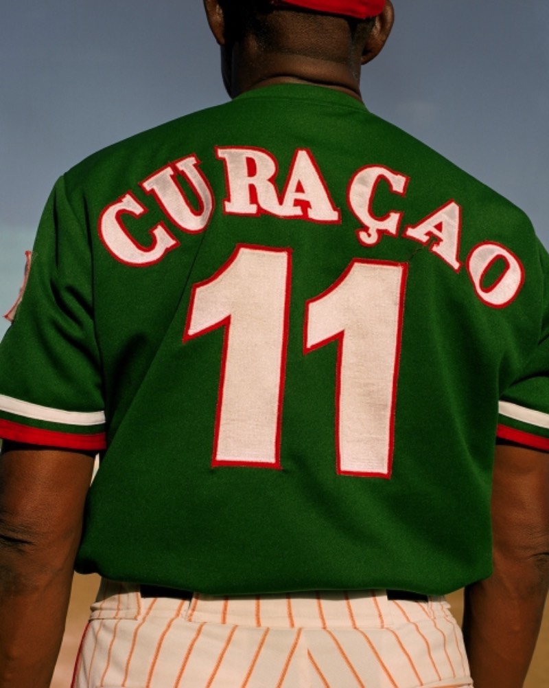 Big Papi é uma série de fotografias de Gilleam Trapenberg onde ele explora os clichês da cultura masculina e como a presença de mulheres independentes e um céu rosa deixa isso tudo de um jeito estranho em Curaçao. Essas cores foram bem aproveitadas pelo fotógrafo que resolveu usar até como temática do projeto, chamando as fotos de uma pesquisa visual na cultura da masculinidade sobreposta contra o pôr do sol da paisagem caribenha. É, Big Papi é uma série de fotos bem interessante no conceito, como que ela acabou ficando visualmente falando?
