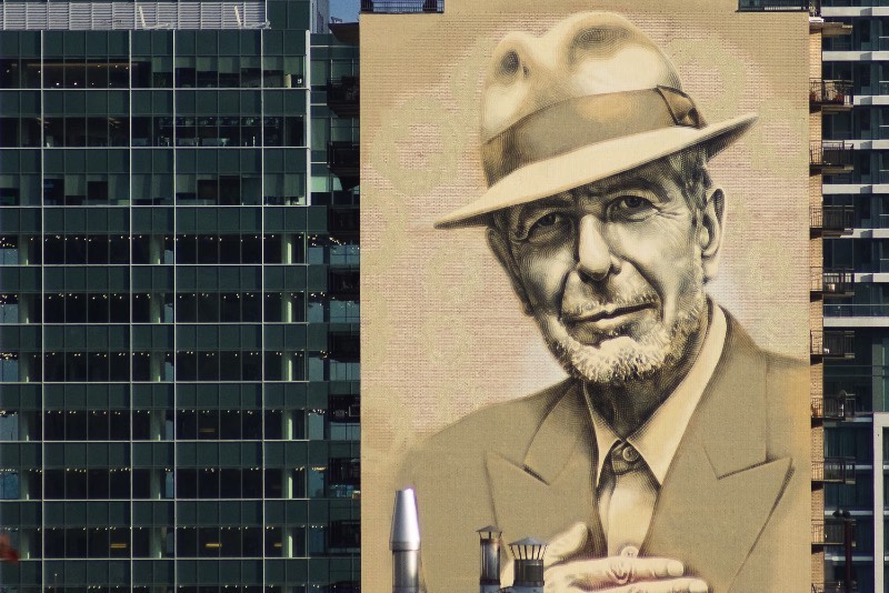 O artista conhecido como El Mac passo um tempo em Montreal, trabalhando para criar um enorme mural para Leonard Cohen em um dos muitos altos prédios da cidade. Esse mural teve a produção e assistência de MU, Gene Penson e um número grande de assistentes que conseguiram colocar em prática o centésimo mural de MU e mais um na coleção de Montreal’s Great Artists. Afinal, o projeto MU quer deixar Montreal mais bonita através de murais e parece que eles estão fazendo isso bem se você olhar as imagens que selecionei para esse artigo.
