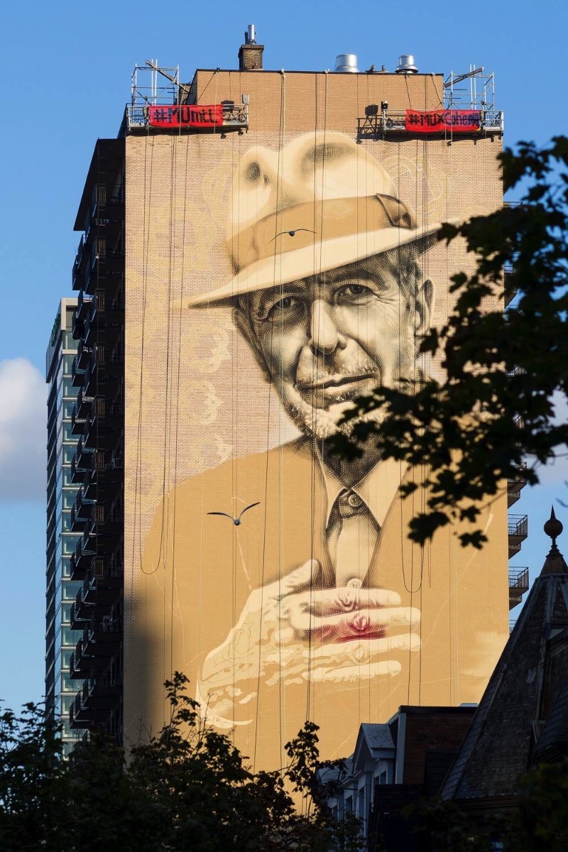 O artista conhecido como El Mac passo um tempo em Montreal, trabalhando para criar um enorme mural para Leonard Cohen em um dos muitos altos prédios da cidade. Esse mural teve a produção e assistência de MU, Gene Penson e um número grande de assistentes que conseguiram colocar em prática o centésimo mural de MU e mais um na coleção de Montreal’s Great Artists. Afinal, o projeto MU quer deixar Montreal mais bonita através de murais e parece que eles estão fazendo isso bem se você olhar as imagens que selecionei para esse artigo.