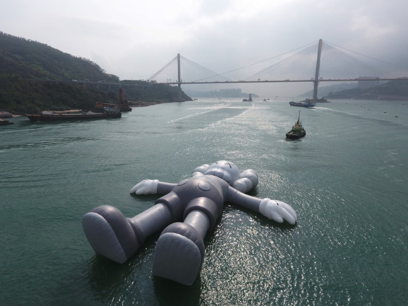 Se você estivesse olhando para o Victoria Harbour de Hong Kong, você veria uma escultura inflável criada pelo artista de rua conhecido como KAWS. Essa cena surreal é realidade, por incrível que pareça. Essa obra monocromática é a maior criação do artista americano e ela foi pensada para representar uma posição de paz, como se ela flutuasse na água olhando para as nuvens e o céu acima de nós. 