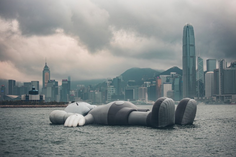 Se você estivesse olhando para o Victoria Harbour de Hong Kong, você veria uma escultura inflável criada pelo artista de rua conhecido como KAWS. Essa cena surreal é realidade, por incrível que pareça. Essa obra monocromática é a maior criação do artista americano e ela foi pensada para representar uma posição de paz, como se ela flutuasse na água olhando para as nuvens e o céu acima de nós. 
