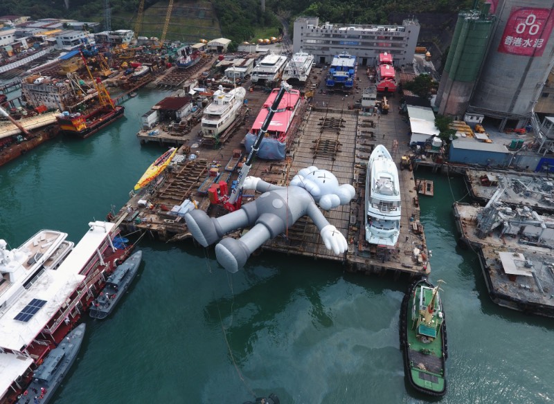 Se você estivesse olhando para o Victoria Harbour de Hong Kong, você veria uma escultura inflável criada pelo artista de rua conhecido como KAWS. Essa cena surreal é realidade, por incrível que pareça. Essa obra monocromática é a maior criação do artista americano e ela foi pensada para representar uma posição de paz, como se ela flutuasse na água olhando para as nuvens e o céu acima de nós. 