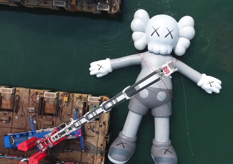 Se você estivesse olhando para o Victoria Harbour de Hong Kong, você veria uma escultura inflável criada pelo artista de rua conhecido como KAWS. Essa cena surreal é realidade, por incrível que pareça. Essa obra monocromática é a maior criação do artista americano e ela foi pensada para representar uma posição de paz, como se ela flutuasse na água olhando para as nuvens e o céu acima de nós. 