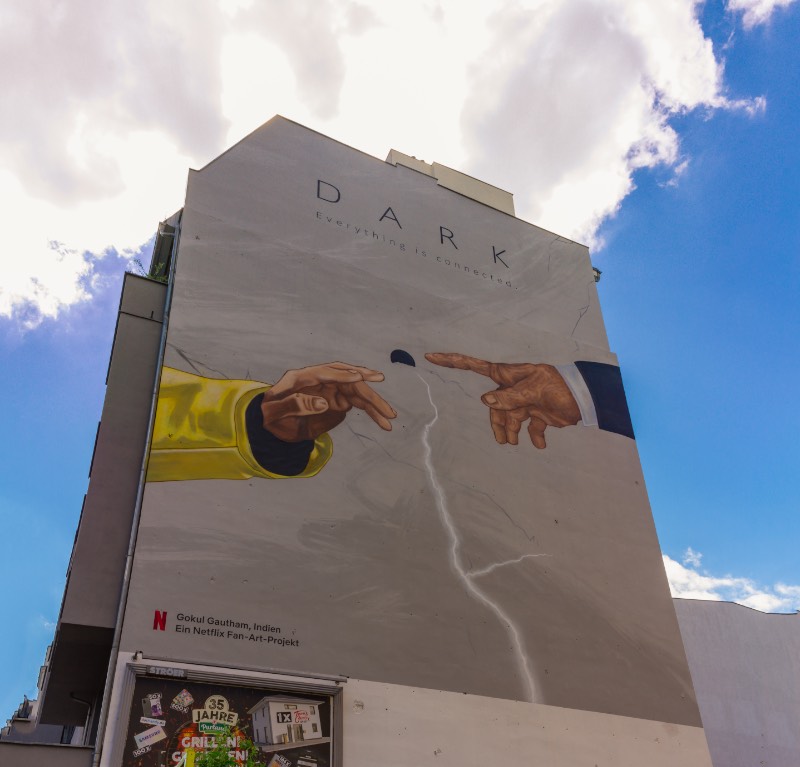 O primeiro mural de Dark em Berlim que eu visitei foi em Prenzlauer Berg, em uma das avenidas que liga o norte da cidade com o centro. Foi lá que eu me deparei com o trabalho de Gokul Gautham que, parece, ter usado de uma referência uma das pinturas mais clássicas da Capela Cistina. Mas, em seu mural, temos as mãos de Jonas e Adam se aproximando perto do que me parece ser uma versão simplificada da caverna. 