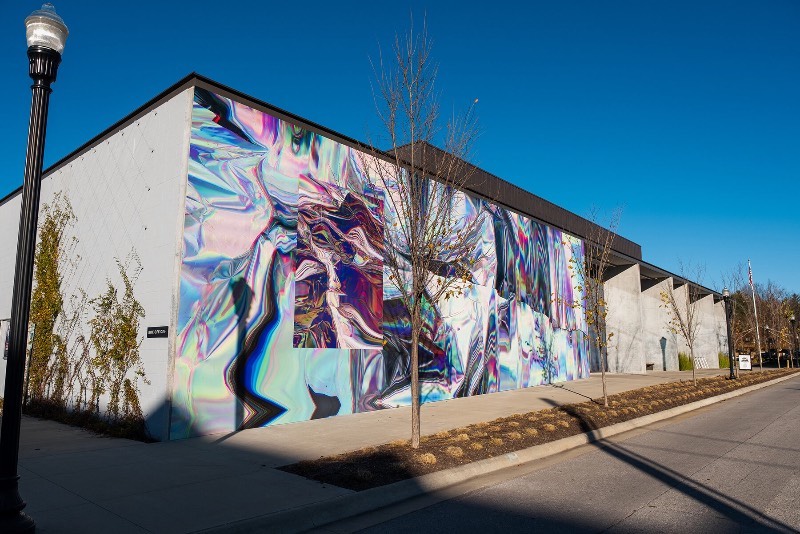 Anne Vieux é uma artista, baseada em Nova Iorque, que recentemente contribui para um projeto de intervenção urbana no centro de Bentonville, no estado americano do Arkansas. Essa instalação de arte de rua consiste em um mural quase holográfico que foi concebido pela artista de forma imersiva já que integra o projeto arquitetônico do prédio ao redor e suas paredes.