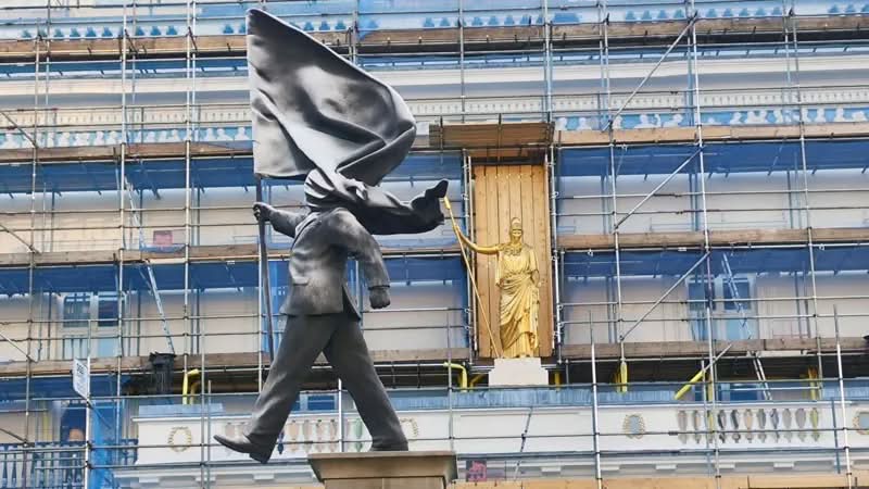 A histórica Waterloo Place, em Londres, é conhecida por seus monumentos a heróis de guerra e à realeza. Mas, no final de abril de 2026, as pessoas que passaram por essa praça foram surpreendidas com uma nova adição à paisagem urbana. Uma estátua do Banksy foi colocada em um pedestal, retratando um homem de terno, cego pela bandeira que carrega, congelado no instante em que parece estar à beira de um precipício.