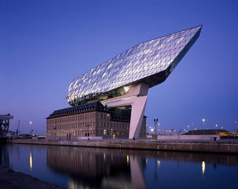 O escritório de arquitetura de Zaha Hadid acabou de inaugurar o novo Port House de Antuérpia, na Bélgica. Essa nova construção usa da estrutura base de uma antiga sede dos bombeiros na zona portuária da cidade e acabou transformando o edifício no centro para os mais de 500 funcionários que trabalhavam em prédios separados pela cidade. A construção foi feita em forma de uma extensão elevada que parece flutuar sobre o edifício original. Sua fachada é feita de vidro com a intenção de refletir as cores do céu e seu formato é inspirado nos navios que cruzam essa cidade belga todos os dias.