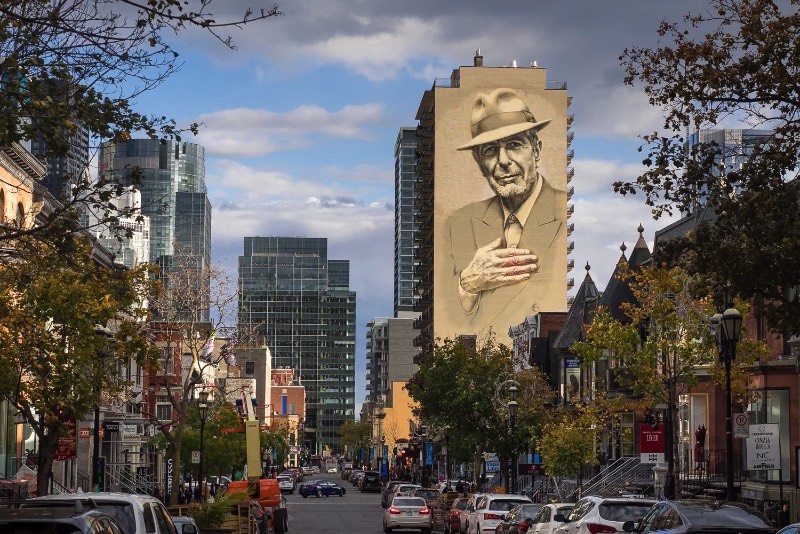 O artista conhecido como El Mac passo um tempo em Montreal, trabalhando para criar um enorme mural para Leonard Cohen em um dos muitos altos prédios da cidade. Esse mural teve a produção e assistência de MU, Gene Penson e um número grande de assistentes que conseguiram colocar em prática o centésimo mural de MU e mais um na coleção de Montreal’s Great Artists. Afinal, o projeto MU quer deixar Montreal mais bonita através de murais e parece que eles estão fazendo isso bem se você olhar as imagens que selecionei para esse artigo.